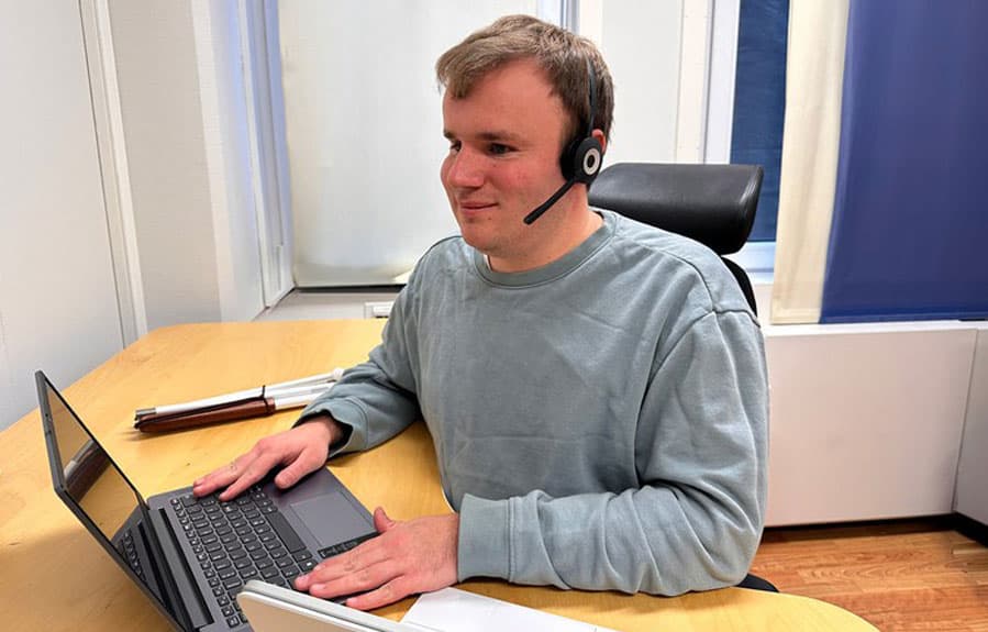 Bilde av en mann med headset som sitter ved en PC 